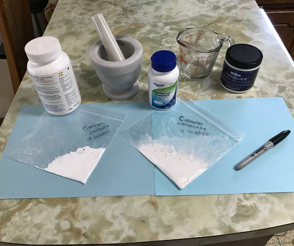 Tabletop with two labeled plastic bags, each filled with a white mixtures, a mortar and pestle, a container of Vaseline, prescription bottles, a measuring glass and a permanent marker.