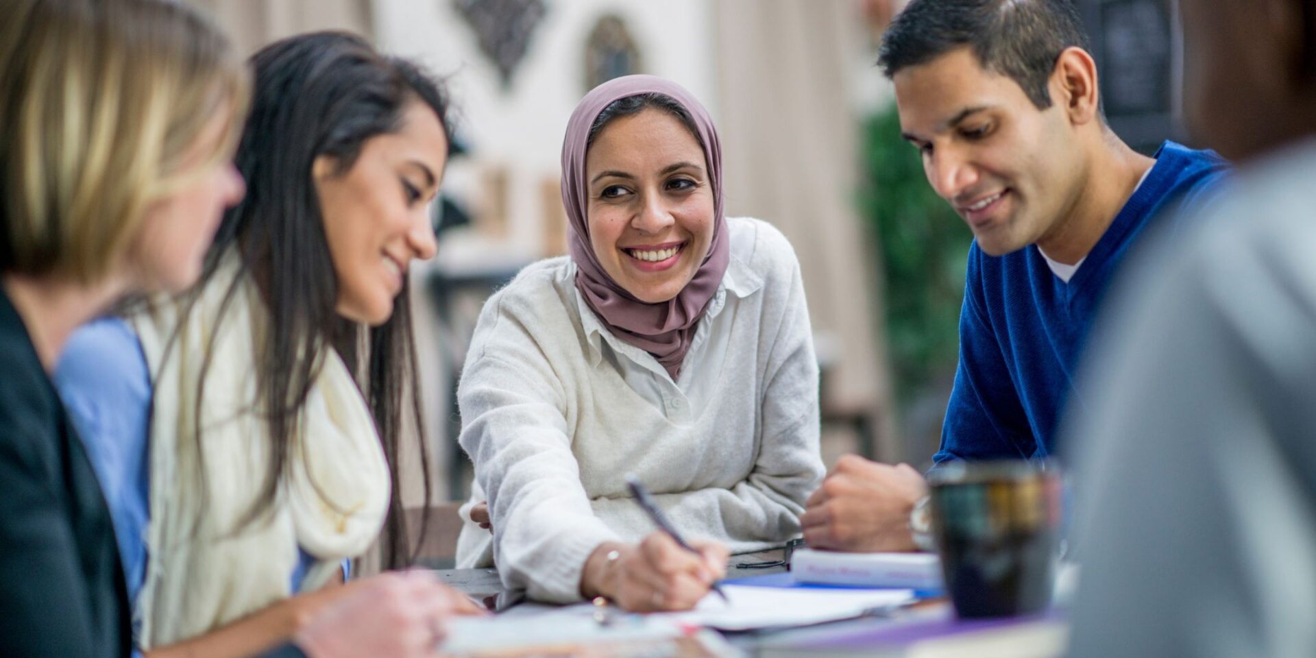 A woman wearing a hijab smiles widely as she speaks to a group sitting around a table. Photo for the art of articulation article.